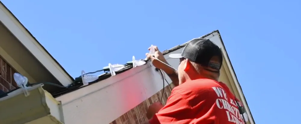 Installer clipping Christmas lights along a roofline gable