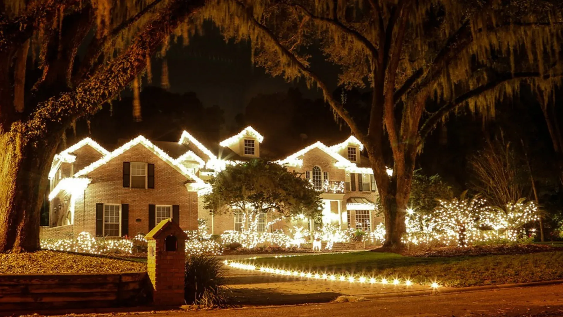 Estate home and oak trees lit with warm white Christmas lights at night